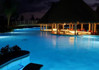 Coco Cay Swimming Pool with swim up bar illuminated under a thatched roof.